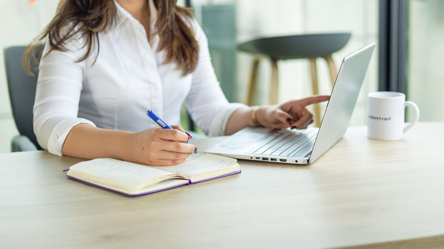 a woman sitting at a desk with a laptop and a notebook